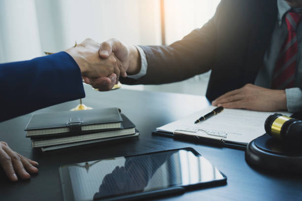 Two businessmen are shaking hands to congratulate a contract agreement gavel tablet balance on the table in a law firm